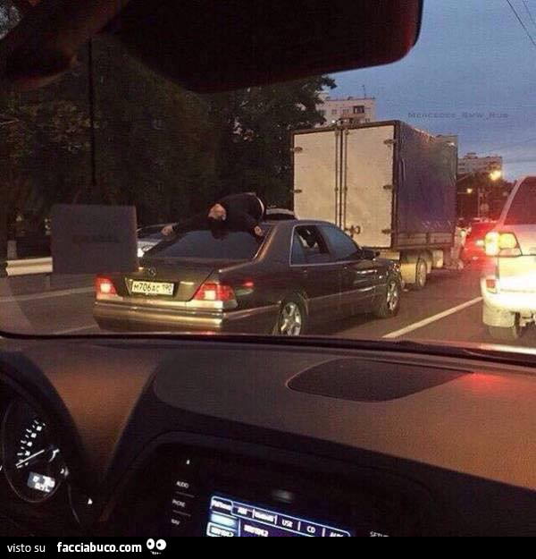 Uomo sdraiato sul tettuccio dell'automobile nel traffico